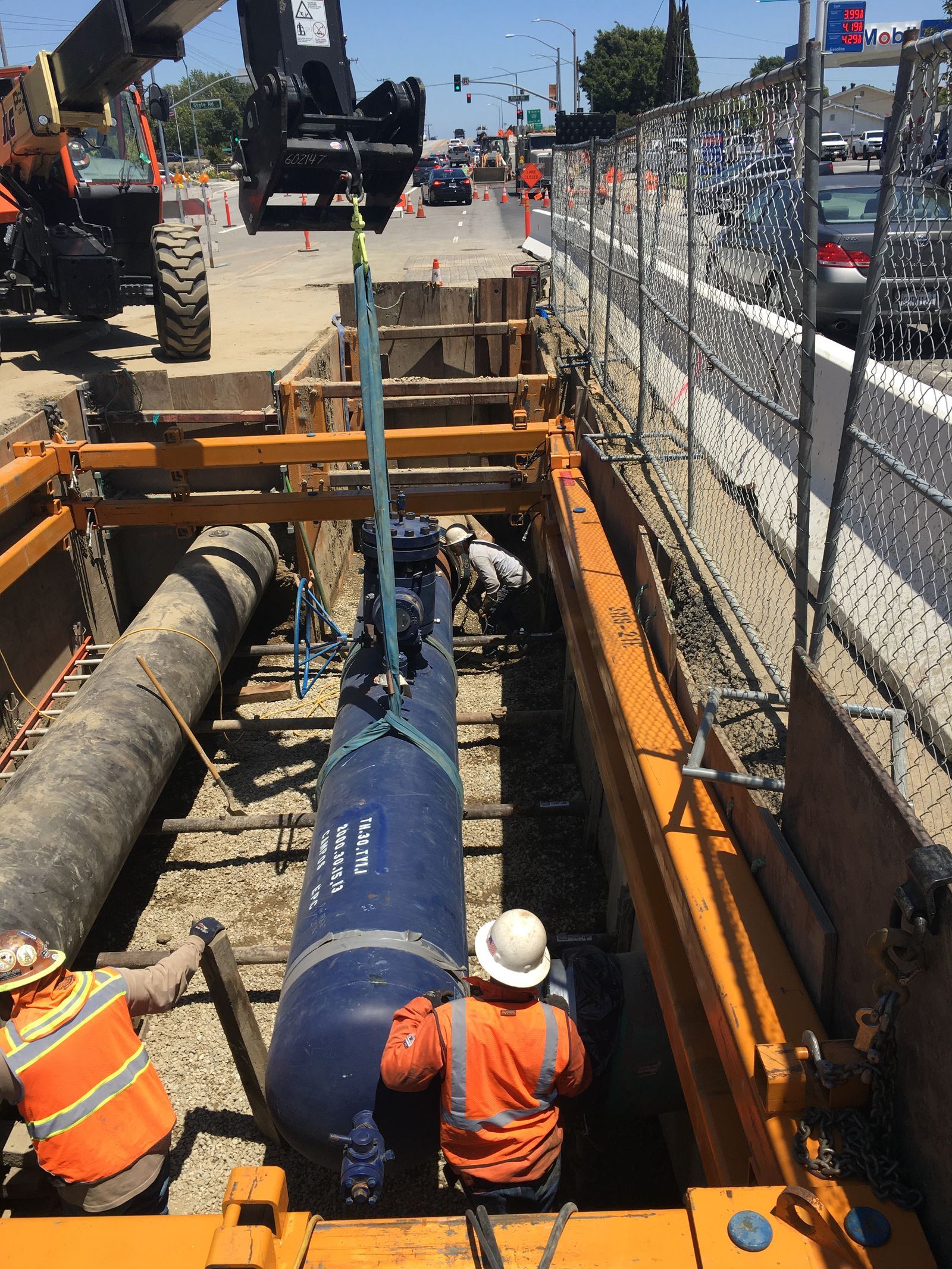 Crew lowering a large-diameter steel pipe into a trench along a city street